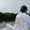 Person wearing black SIC Distressed Ball Cap from the back while seated on a boat