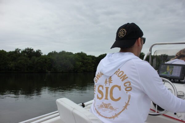 Person wearing black SIC Distressed Ball Cap from the back while seated on a boat