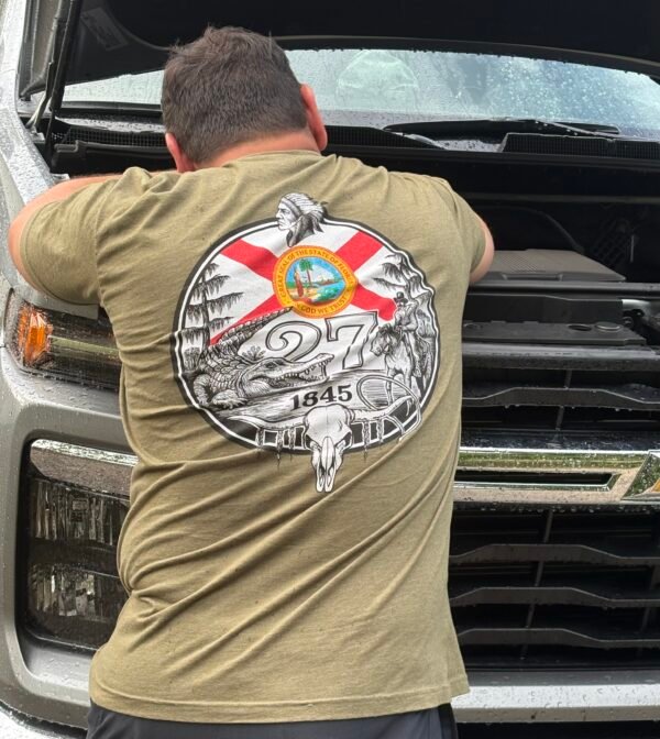 Person wearing Military Green Florida 27th State T-Shirt with Florida 27th State back artwork while working on a truck